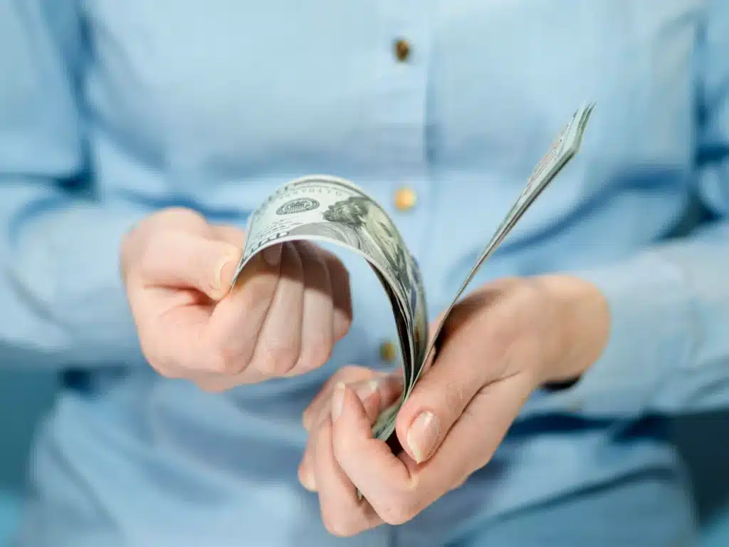 Pessoa contando notas de dólar com as mãos, vestindo camisa azul.