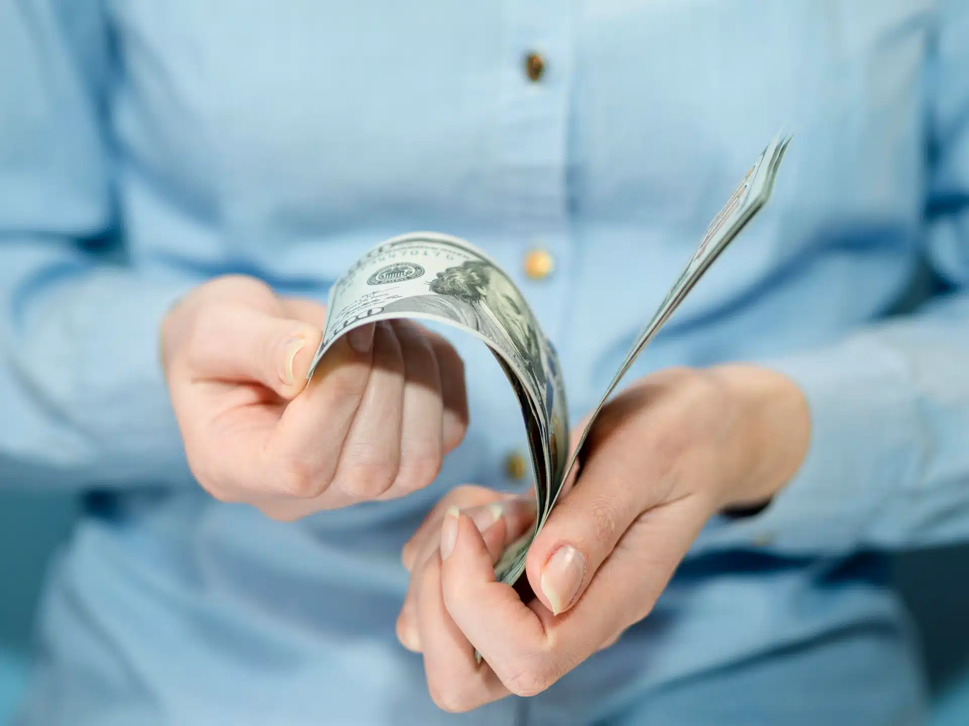 Pessoa contando notas de dólar com as mãos, vestindo camisa azul.