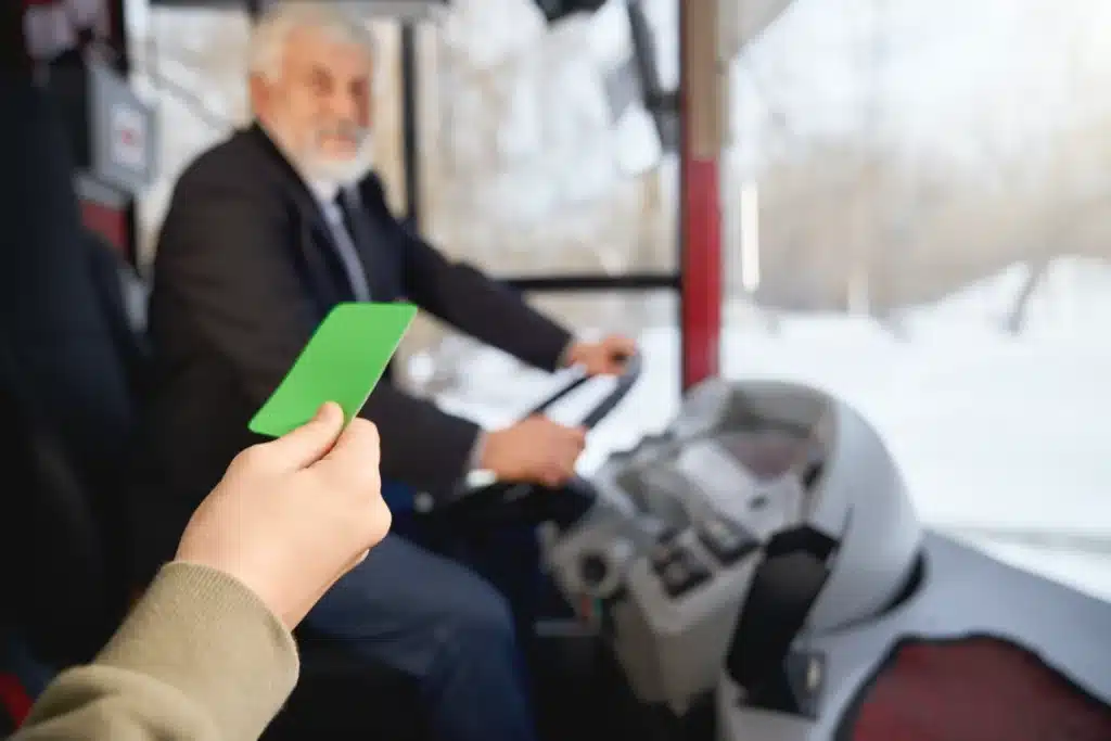 Pessoa apresentando um cartão verde ao motorista, enquanto entra em um ônibus
