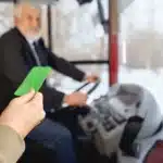 Pessoa apresentando um cartão verde ao motorista, enquanto entra em um ônibus